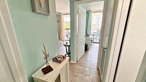 Un couloir étroit avec une console blanche, un tableau encadré et une porte donnant sur un balcon.