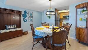 A dining area with a round table, wicker chairs, and a ceiling light. - Castle Reef 213 stunning ocean views (New Smyrna Beach)