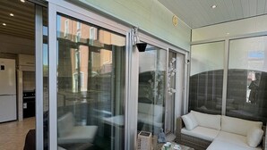 A modern outdoor seating area with wicker furniture and glass doors leading to a kitchen. - Pleasant apartment on the ground floor 4DAUP4 (LE BARCARES)