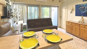 A dining area with a wooden table set for four, a sofa, and a cabinet with decorative items. - Pleasant apartment on the ground floor 4DAUP4 (LE BARCARES)
