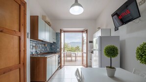 Une cuisine moderne avec des meubles en bois, un coin repas avec une table et des chaises, une plante en pot et un téléviseur affichant le logo « NETFLIX ».