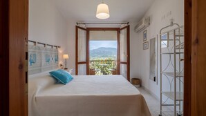 Une chambre avec un lit, un balcon offrant une vue sur les montagnes, un luminaire suspendu et un plafond blanc.