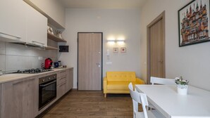 A compact kitchen with a gas stove, oven, and wooden cabinets. There is a yellow sofa and a white dining table with chairs.