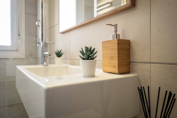 Un baño con un lavamanos blanco, un dispensador de jabón de madera y una pequeña planta en maceta.