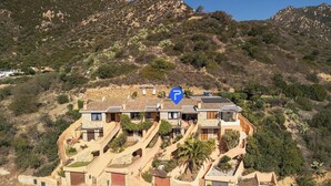 Una proprietà su una collina con diversi edifici, tra cui una casa principale con tetto in tegole e una struttura più piccola con tetto di paglia.
