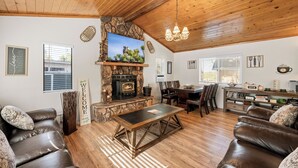 Una sala de estar con chimenea de piedra, sofás de cuero, una mesa de centro de madera y un comedor con sillas y una mesa.