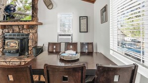 Un comedor con chimenea de piedra, televisor y un amplio ventanal con persianas.