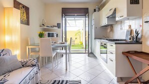 Una cocina moderna con armarios blancos, una zona de comedor con mesa y sillas, y una sala de estar con sofá.