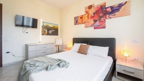 Un dormitorio moderno con cama, mesitas de noche, televisor y una obra de arte en la pared.