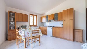 A compact kitchen with wooden cabinets, a dining table set for four, and a small refrigerator. - Relax Sea Home by Propertize - Villasimius (Villasimius)