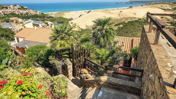Vista costera con playa, una escalera de piedra y una valla de madera.