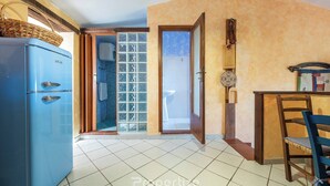 Una cocina con un refrigerador azul, un comedor con mesa y sillas de madera, y un baño con puerta de vidrio.