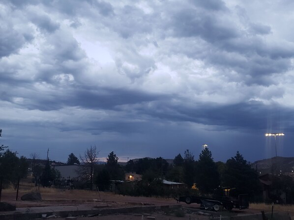 A rural landscape with a cloudy sky, a parked truck, and a house with lights on.
