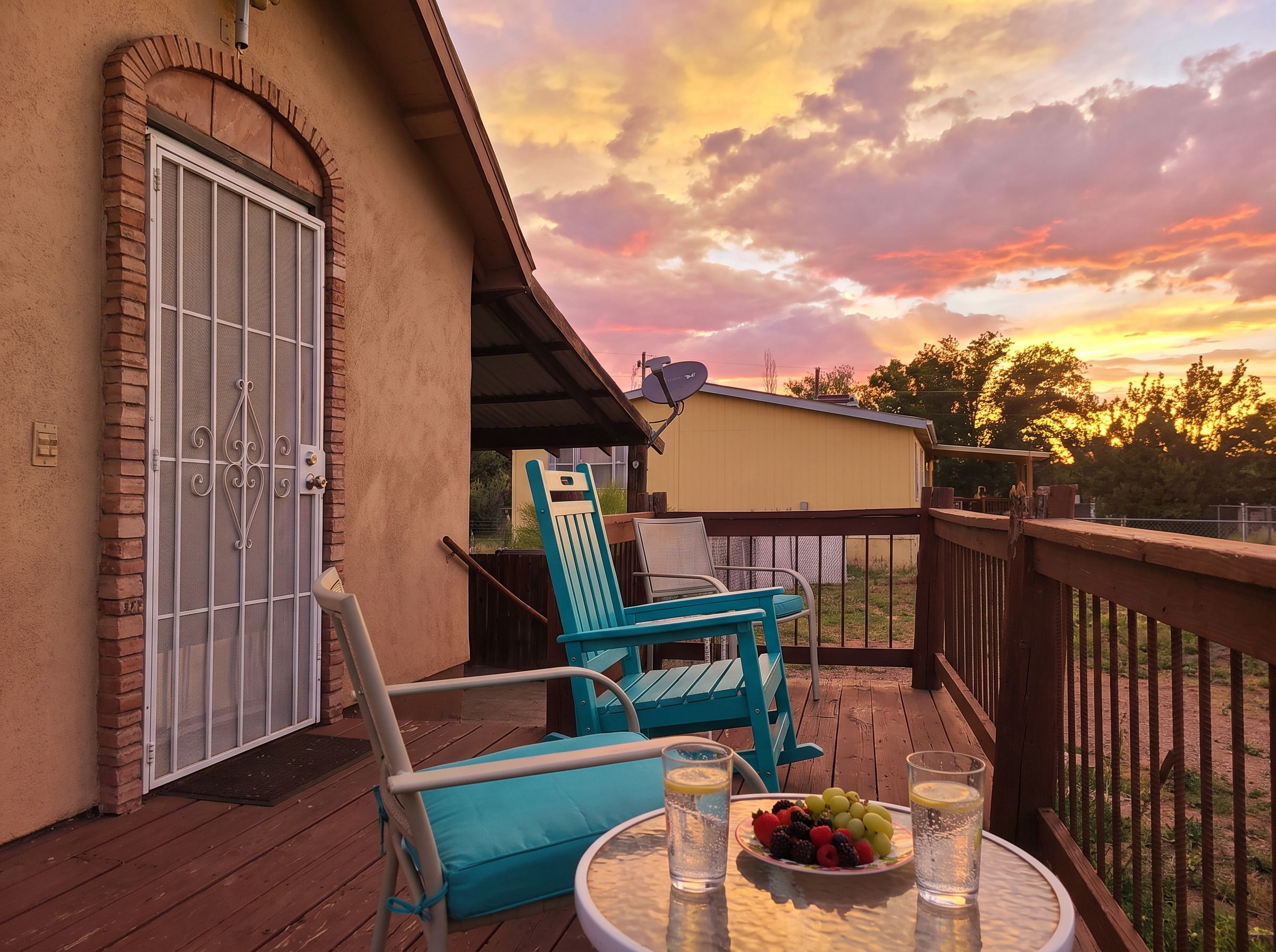 A wooden deck with a table set for two, a blue chair, and a covered patio area.