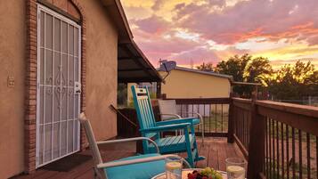 A wooden deck with a table set for two, a blue chair, and a covered patio area.