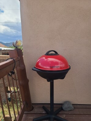 A Cuisinart grill on a wooden deck with a railing, a stone, and a view of mountains.