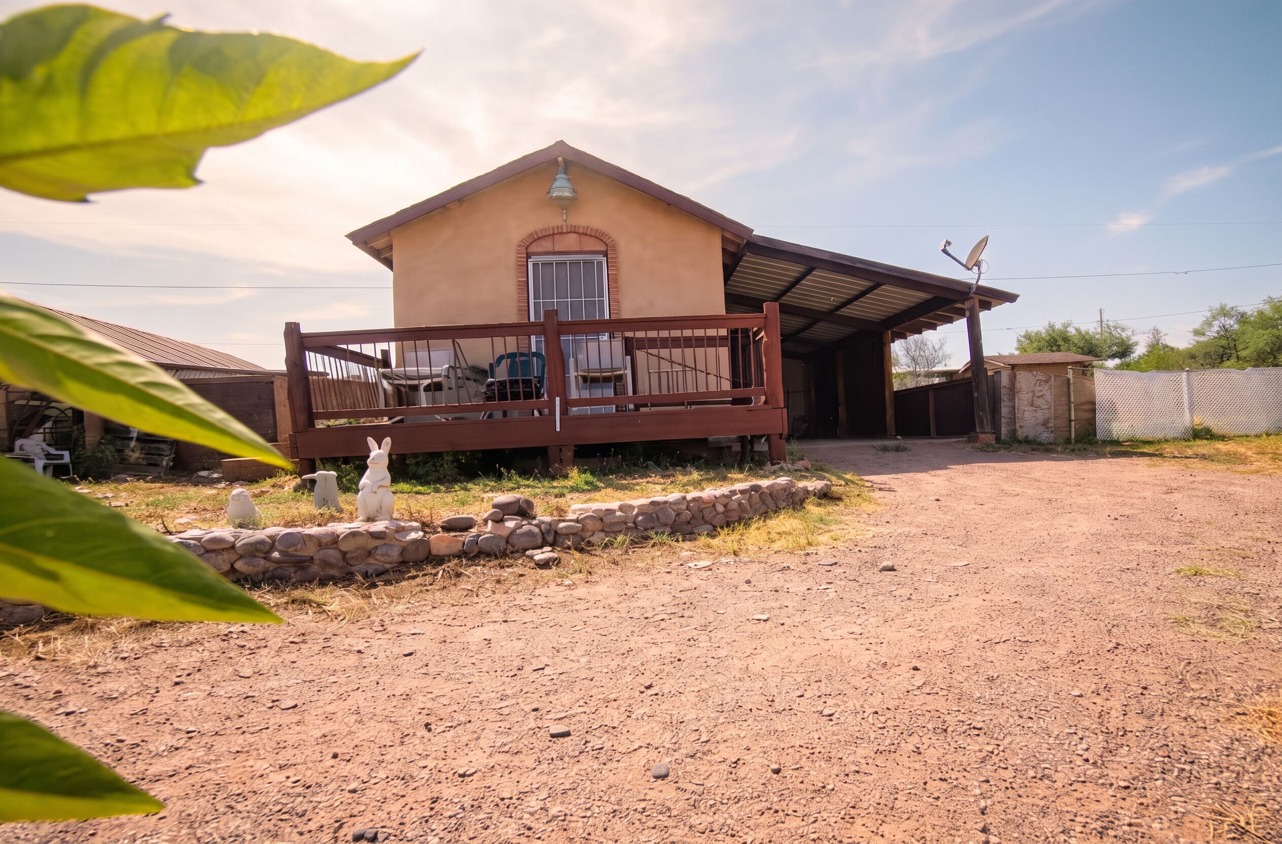 A single-story house with a porch, a satellite dish, and a stone wall.