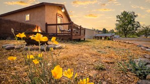 Una cabaña rústica con un hogar, rodeada por un paisaje árido con flores amarillas.