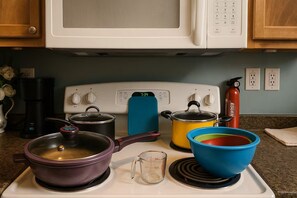 A kitchen with a stove, pots, a coffee maker, and a fire extinguisher.