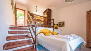 A bedroom with a bed, a wooden staircase, and a view of the outdoors.