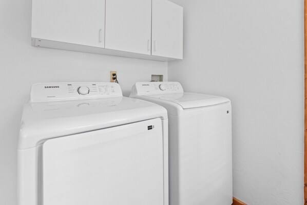 A laundry room with two white Samsung front-loading washers and a white cabinet above them.
