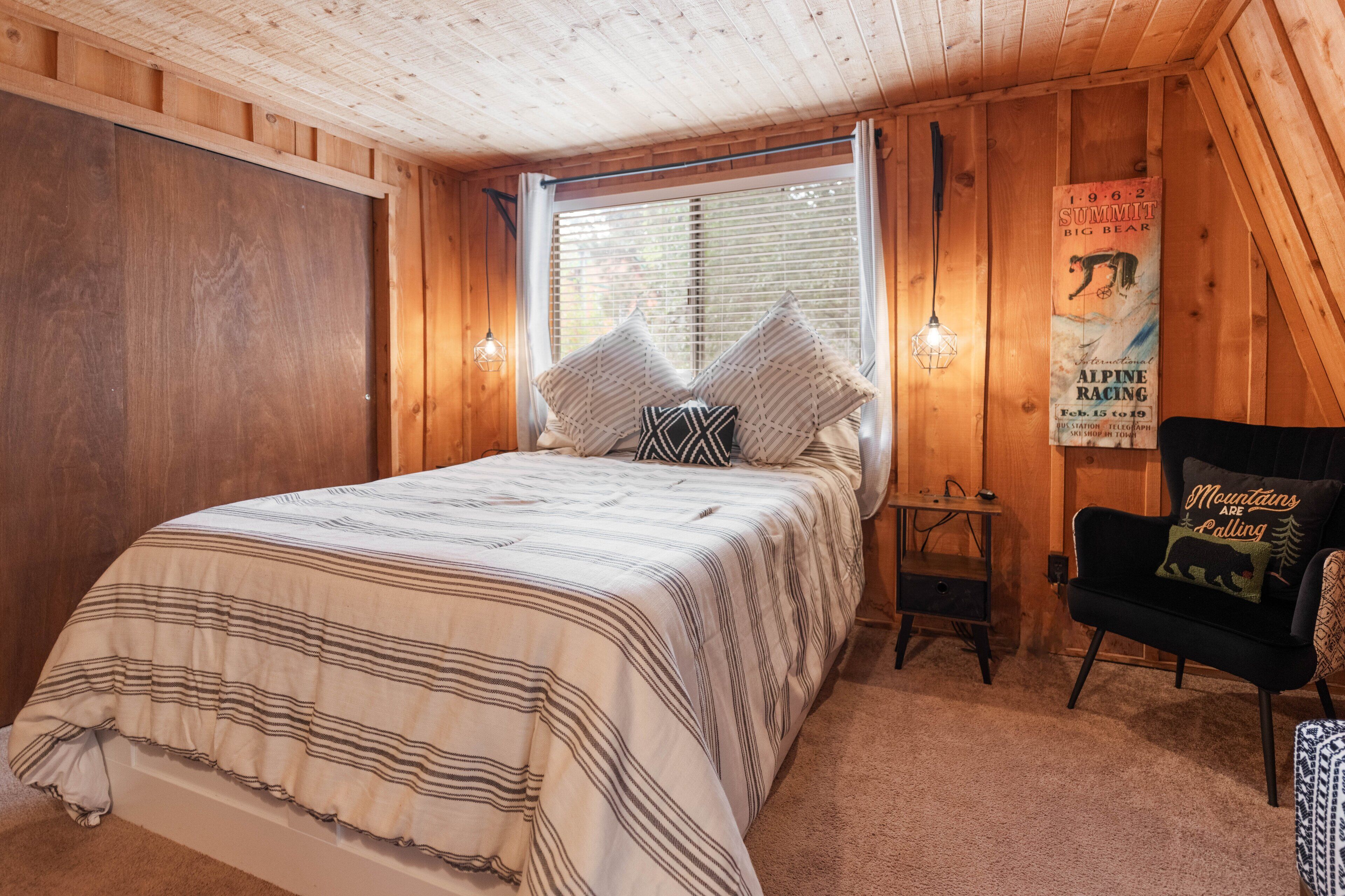 A wooden cabin bedroom with a bed, a chair, a poster, and a window with blinds.