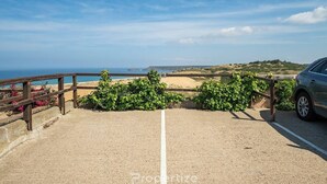 Ein gepflasterter Weg führt zu einem Strand, wo ein Holzzaun steht und ein Auto am Rand geparkt ist.