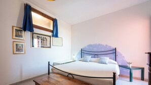 Ein Schlafzimmer mit einem Bett, einem Nachttisch, einem kleinen Tisch und einem Fenster mit Vorhängen.