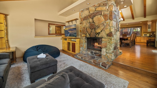 A spacious living room with a stone fireplace, wooden beams, and a cozy seating area. - Moonridge Retreat - 6BR, Walk to Bear Mountain, Foosball Table, BBQ (Big Bear Lake)
