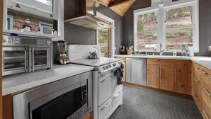 Een moderne keuken met een inbouwoven, magnetron en kookplaat. De keuken heeft houten kastjes, een groot raam en uitzicht op het buitengebied.
