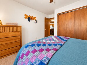 A bedroom with a wooden dresser, a quilted bedspread, and a wooden wardrobe.