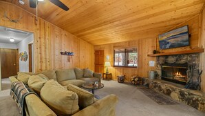 Ein gemütliches Blockhaus-Interieur mit Kamin, einer Couch und einem Deckenventilator.