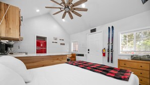 Ein Schlafzimmer mit Bett, Holz-Kopfbrett, Deckenventilator, Skiausrüstung und einem Fenster mit Jalousien.