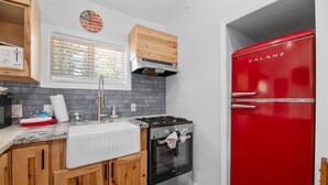 Eine Küche mit Holzausstattung, einem roten Kühlschrank, einem Herd und einem Fenster mit Jalousien.