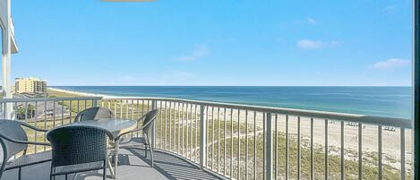 Un balcon avec vue sur la plage et l’océan, comprenant une table et des chaises.