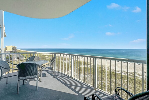 A balcony with a view of the beach and ocean, featuring a table and chairs.