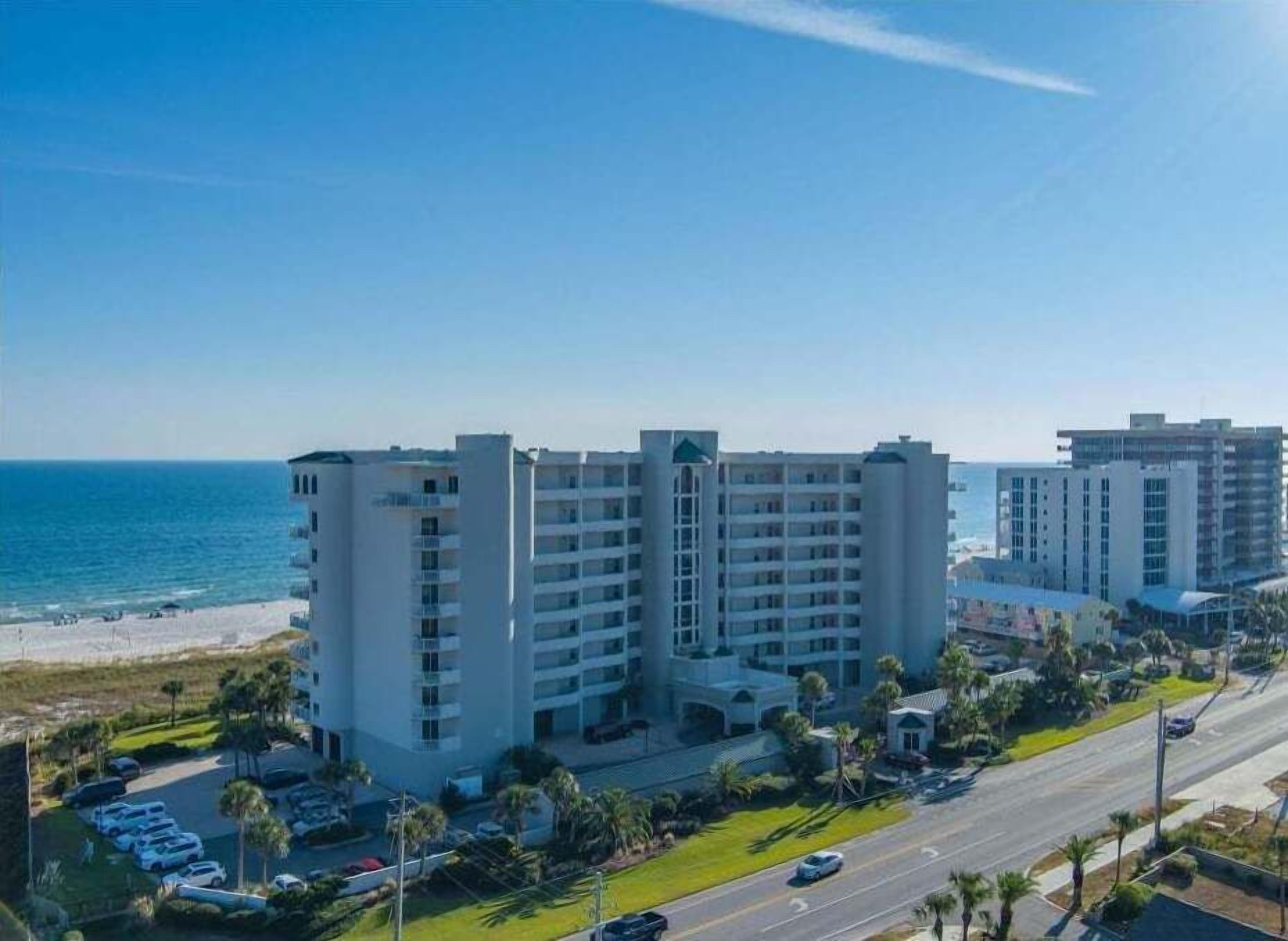 A beachfront hotel with multiple floors, a parking lot, and a view of the ocean.