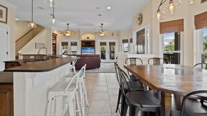 A spacious kitchen with a large island, modern pendant lights, and a view to the living area.