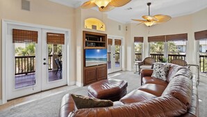 A spacious living room with a leather sofa, a flat-screen TV, and a ceiling fan.