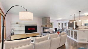 A modern living room with a fireplace, a TV displaying 'NETFLIX', and a cozy seating area. - Saltwater Pool |Outdoor Kitchen, Bar & TV |Poolside Seating |Gas Fireplace |Near Downtown (Lake Geneva)