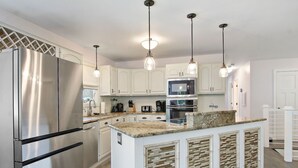 A modern kitchen with stainless steel appliances, white cabinetry, and a central island with a mosaic backsplash. - Saltwater Pool |Outdoor Kitchen, Bar & TV |Poolside Seating |Gas Fireplace |Near Downtown (Lake Geneva)