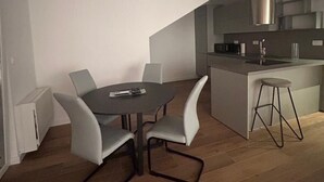 Una cocina moderna con una isla central, un comedor con mesa y sillas, y una escalera que conduce a un nivel superior.