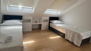 Habitación pequeña con dos camas, un escritorio y tragaluces.