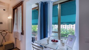 Un balcon avec une table dressée pour le petit-déjeuner, une pancarte d’accueil encadrée et une vue sur les bâtiments et les arbres.