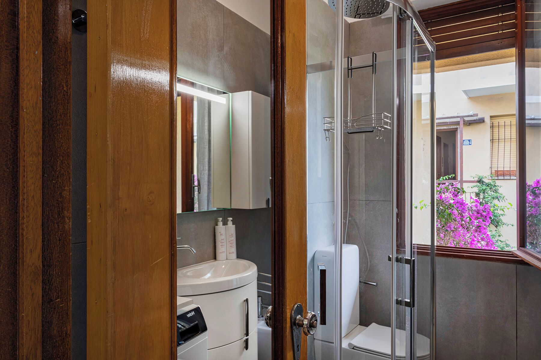 Een moderne badkamer met een douchecabine van glas, een toilet en een wastafel met een spiegel erboven.
