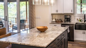 A kitchen with white cabinets, a granite countertop, and a wooden bowl. - Spacious & Modern Rumbling Bald Retreat! Hot Tub, Fire Pit, Game Room (Lake Lure)