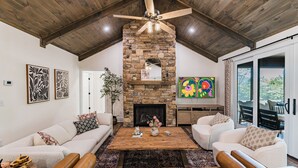 A spacious living room with a stone fireplace, leather sofas, and a wooden ceiling fan. - Spacious & Modern Rumbling Bald Retreat! Hot Tub, Fire Pit, Game Room (Lake Lure)