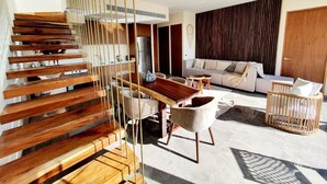 A modern living room with a wooden staircase, a sofa set, and a dining area. - Penthouse de Lujo con 3 Recamaras, Baños, Sala Comedor, Cocina, Jacuzzi Privado (Tulum)