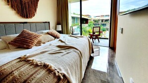 A modern hotel room with a large bed, a view of the outdoor balcony, and a decorative wall hanging. - Penthouse de Lujo con 3 Recamaras, Baños, Sala Comedor, Cocina, Jacuzzi Privado (Tulum)