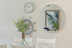 Een eethoek met een ronde spiegel, een wandklok en een plant in een glazen vaas.